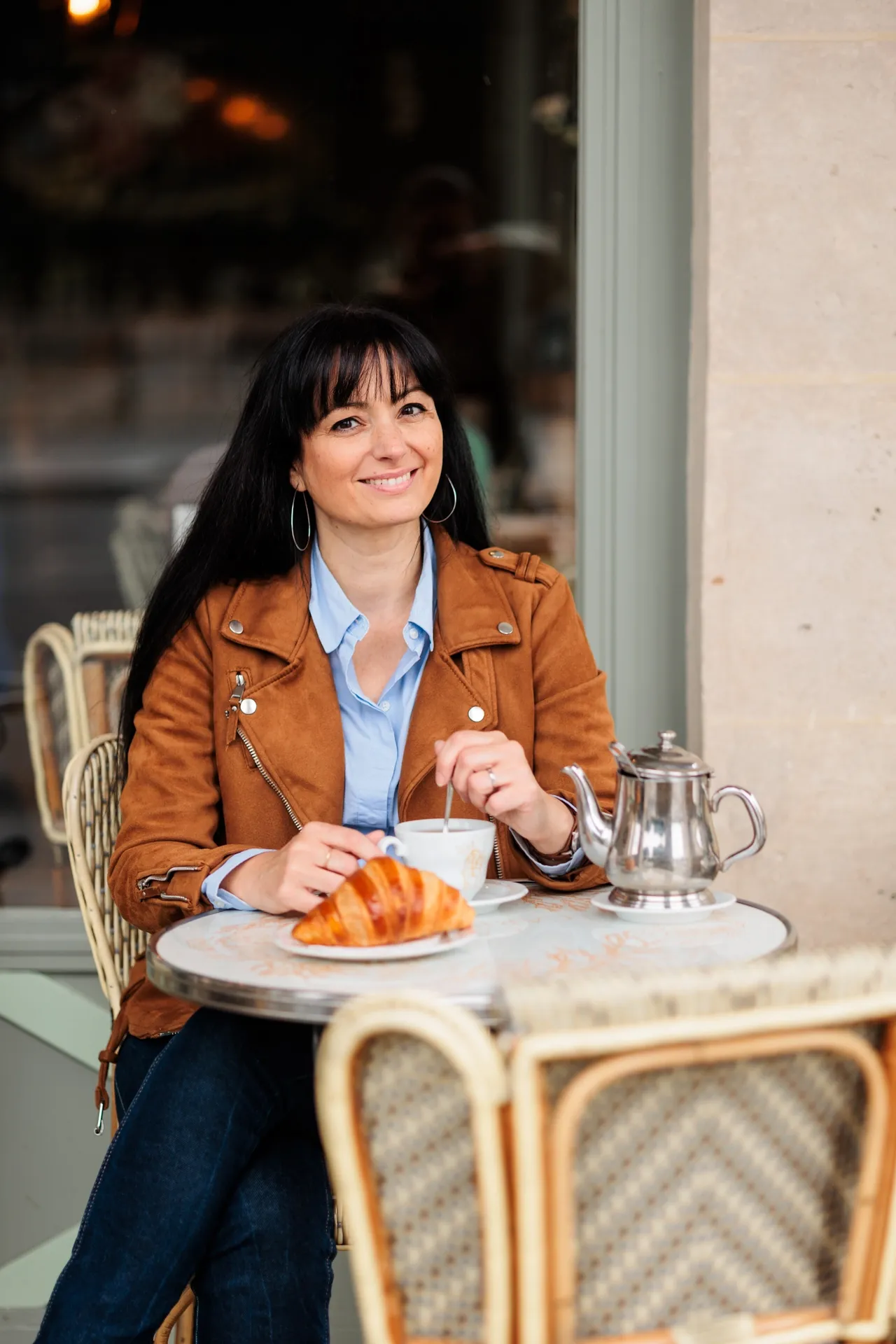 Entrepreneuse souriante en terrasse à Paris, café et croissant sur la table, pendant sa séance personal branding